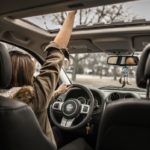 woman raising her right hand inside black and brown vehicle